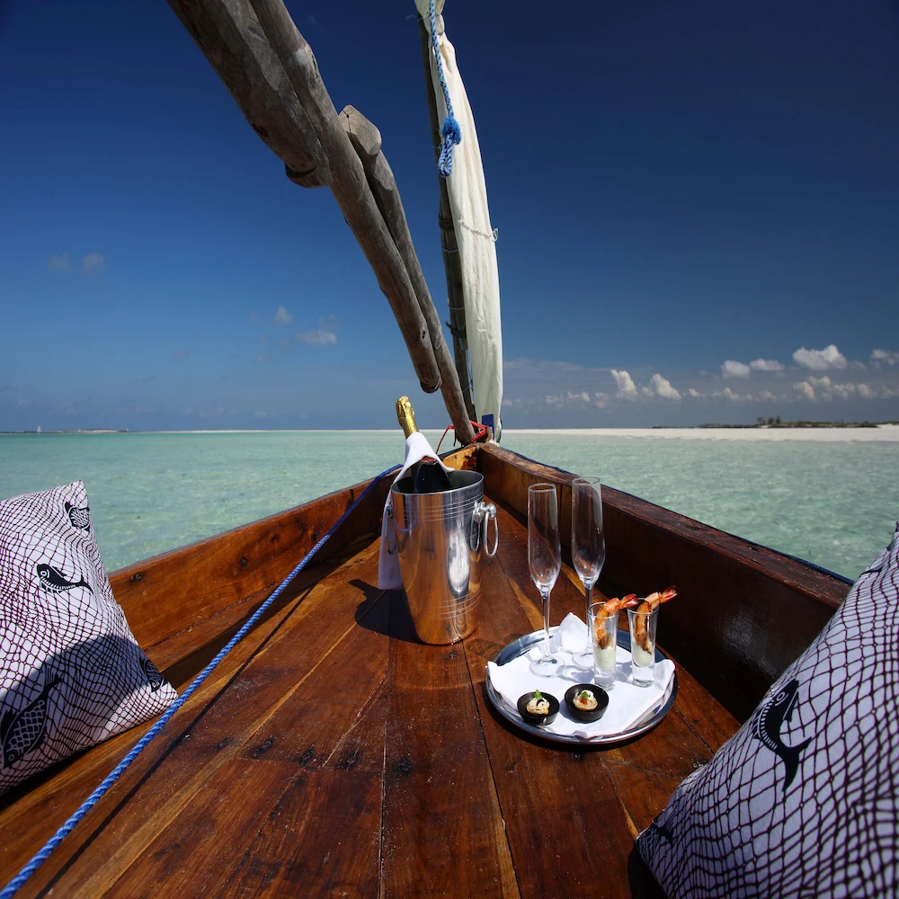 Relaxing dhow cruise experience on the Indian Ocean in Mozambique, with drinks served on a traditional wooden boat surrounded by crystal-clear waters and blue skies.