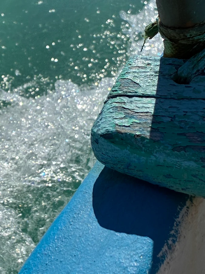 Side view of a boat floating on the crystal-clear turquoise waters of the Indian Ocean near Vilanculos, with sunlight reflecting off the calm sea and the horizon stretching into a bright blue sky