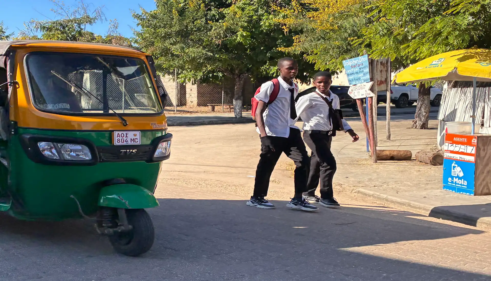 Young school boys walking on the streets in Vilanculos Mozambique with a Tuktuk on the raod