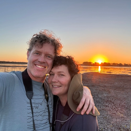 A couple standing together on the open plains of Zinave National Park in Mozambique as the sun sets, casting warm golden light across the landscape.