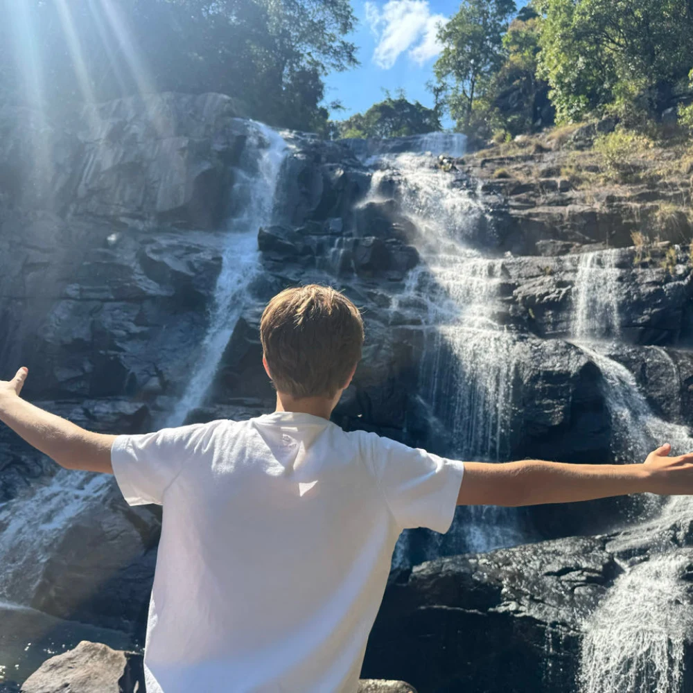 Waterfall Mount Gorongosa A boy standing beside a waterfall on Mount Gorongosa in Mozambique, surrounded by lush wilderness